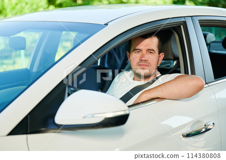 Adult man looking through window of his car. Confident man looking straight into the camera while sitting in white car. 114380808