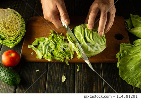 Chef hands with a knife while cooking on a kitchen black table. Delicious salad for breakfast with fresh vegetables by the hands of the cook 114381291