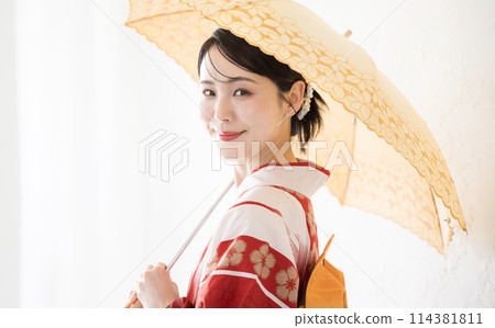 一位穿著浴衣、撐著遮陽傘的可愛日本女人，穿著日本和服看著鏡頭，以度過夏日的陽光 114381811