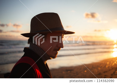 Golden hour stroll man walks along tranquil seashore. 114382090