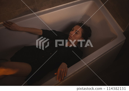 Desperate woman sitting with arms resting on bathtub rim. 114382131