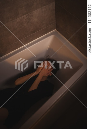 Tearful woman submerged in bathtub, eyes closed. 114382132