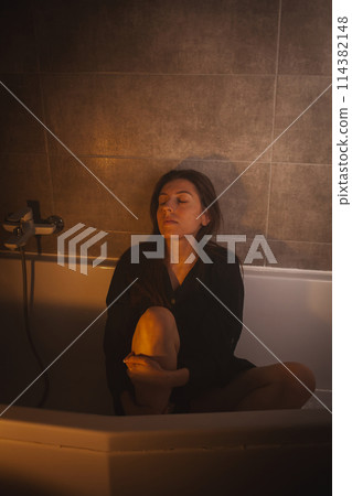 Worried woman curled up in empty bathtub. 114382148