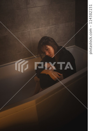 Sad woman sitting with knees drawn up in tub. Sad woman sitting with knees drawn up in tub. 114382151