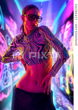 Vibrant street style. Portrait of woman wearing uniquely top and trendy eyeglasses, with vividly colorful neon graffiti background. Vibrant street style. Portrait of woman wearing uniquely top and trendy eyeglasses, with vividly colorful neon graffiti background. 114382301