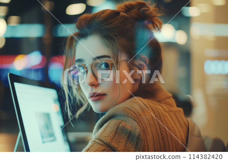 Portrait of employee young woman in glasses working on laptop in the office looking at camera Portrait of employee young woman in glasses working on laptop in the office looking at camera 114382420