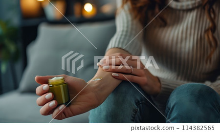 Casual woman in cozy setting applies ointment for skincare or medical use. Relaxed home wellness routine. Personal health care moment. AI 114382565