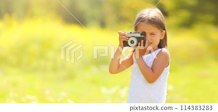 Child with film camera taking picture outdoors on sunny summer day Child with film camera taking picture outdoors on sunny summer day 114383283