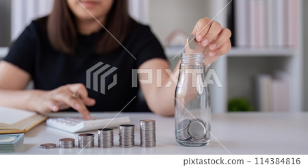 Woman saving money with hand putting coins in jug glass concept finance and accounting finance and saving money for future concept 114384816