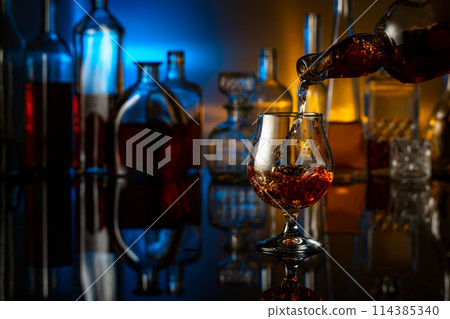 Brandy is poured from a bottle into a glass. 114385340