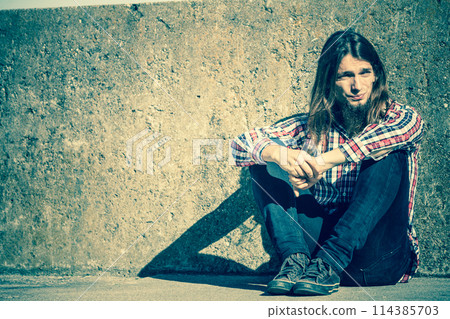 Man long haired sitting alone sad on grunge wall 114385703