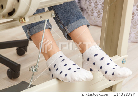 Female feet on the pedal of a sewing machine, motor 114388387