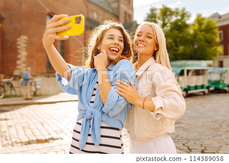 Happy women taking selfie while walking down street. Fashion, travel, technology, blogging concept. Happy women taking selfie while walking down street. Fashion, travel, technology, blogging concept. 114389058