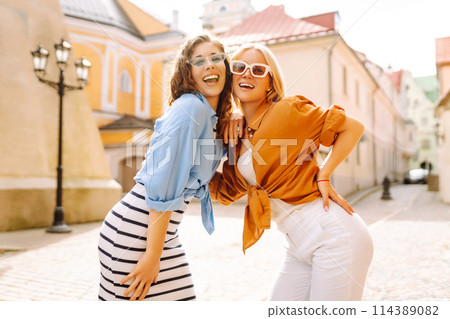 Two young women in trendy summer clothes posing on the street background. Concept of lifestyle. 114389082