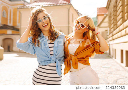 Two young women in trendy summer clothes posing on the street background. Concept of lifestyle. 114389083