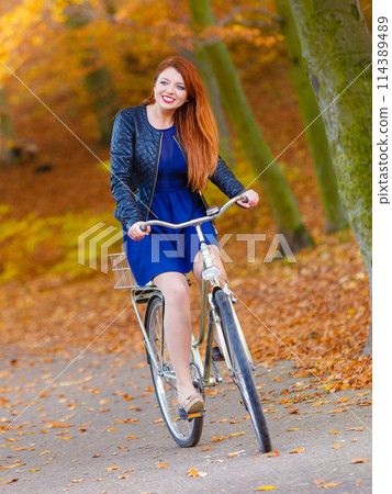 Redhead lady cycling in park. 114389489