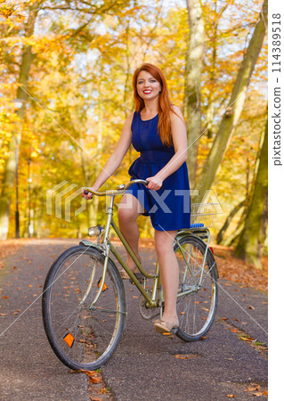 Redhead lady cycling in park. Redhead lady cycling in park. 114389518