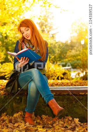 woman girl relaxing in autumnal park reading book 114389527