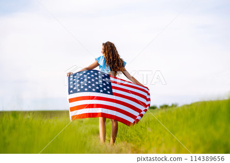 Young woman with american USA flag on blooming meadow. Independence Day, 4th July. Young woman with american USA flag on blooming meadow. Independence Day, 4th July. 114389656