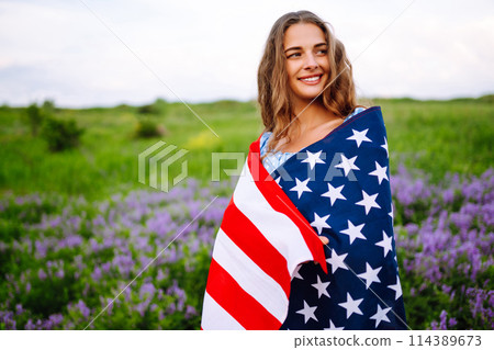 Young woman with american USA flag on blooming meadow. Independence Day, 4th July. Young woman with american USA flag on blooming meadow. Independence Day, 4th July. 114389673