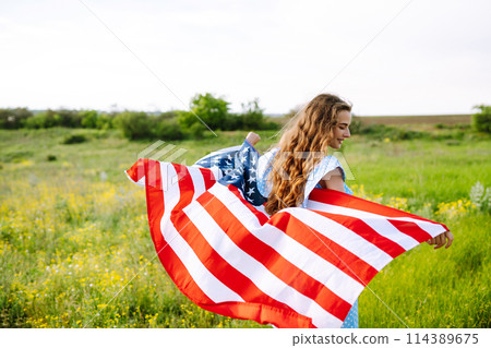 Young woman with american USA flag on blooming meadow. Independence Day, 4th July. Young woman with american USA flag on blooming meadow. Independence Day, 4th July. 114389675