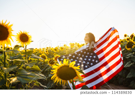 Woman proudly hold waving american USA flag in in the sunflower field. Independence Day, 4th July. Woman proudly hold waving american USA flag in in the sunflower field. Independence Day, 4th July. 114389830