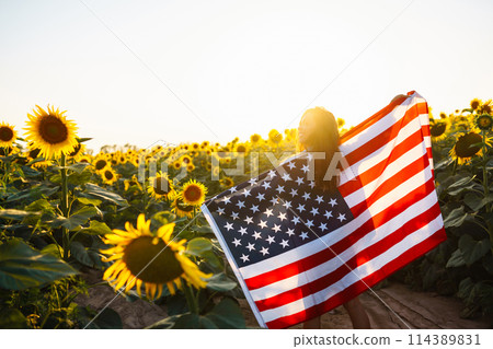Woman proudly hold waving american USA flag in in the sunflower field. Independence Day, 4th July. Woman proudly hold waving american USA flag in in the sunflower field. Independence Day, 4th July. 114389831