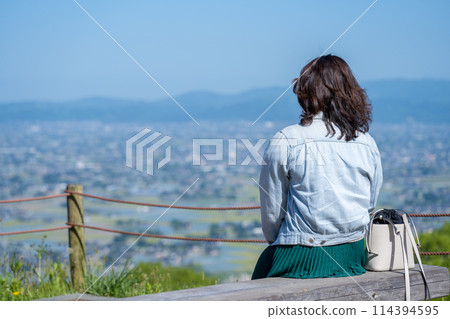 Image of a woman sitting on a bench and the vast Tonami Plain in spring | Photographed from the Sankyomura Observatory | Tonami City, Toyama Prefecture Image of a woman sitting on a bench and the vast Tonami Plain in spring | Photographed from the Sankyomura Observatory | Tonami City, Toyama Prefecture 114394595