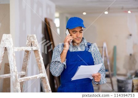 Young foreman with documents in his hands is talking on a mobile phone 114394753