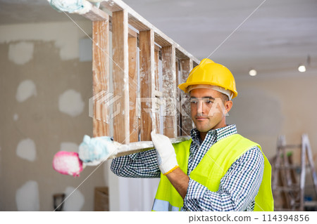 Construction worker carrying stepladder in apartment 114394856
