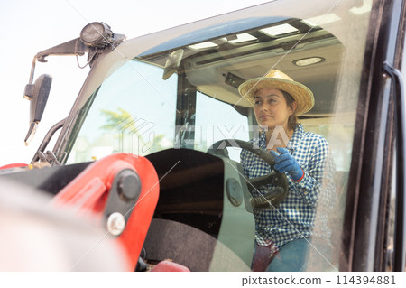Portrait of a young woman farmer sitting at the wheel of a tractor 114394881