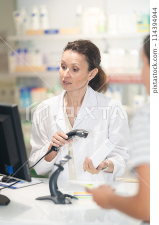 Middle-aged female pharmacist scanning barcode on medicine box Middle-aged female pharmacist scanning barcode on medicine box 114394944
