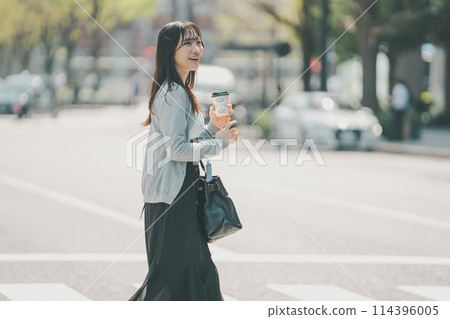 一個 20 多歲的女人，笑容可愛，端著外帶咖啡在城市裡散步 114396005