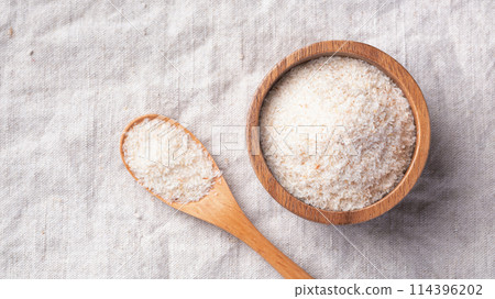 Psyllium husk in wood bowl with spoon on linen table cloth background, top view, copy space 114396202