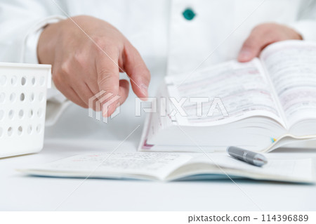 A pharmacist checking the safety of medicines in a prescription book by looking at the manual A pharmacist checking the safety of medicines in a prescription book by looking at the manual 114396889