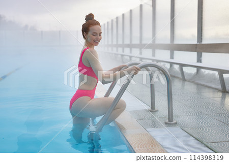 ginger female entering swimming pool and looking down 114398319