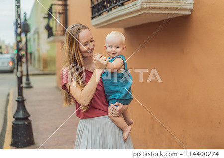 Mother and baby son tourists explore the vibrant streets of Valladolid, Mexico, immersing herself in the rich culture and colorful architecture of this charming colonial town 114400274