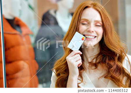 smiling beautiful girl with long red hair is happy to use cashback 114400312