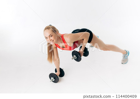 sporty woman doing press ups with dumbbells in the gym 114400409