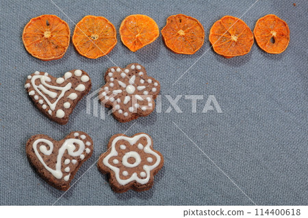 Gingerbread cookies decorated with a pattern of white glaze. On a background of gray fabric. Decorated with decorative elements of dried fruit Gingerbread cookies decorated with a pattern of white glaze. On a background of gray fabric. Decorated with decorative elements of dried fruit 114400618