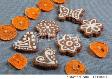 Gingerbread cookies decorated with a pattern of white glaze. On a background of gray fabric. Decorated with decorative elements of dried fruit Gingerbread cookies decorated with a pattern of white glaze. On a background of gray fabric. Decorated with decorative elements of dried fruit 114400619