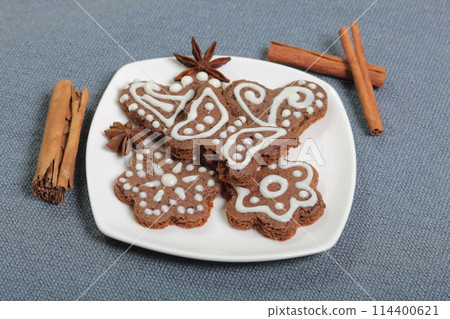 Gingerbread cookies decorated with a pattern of white glaze. On a background of gray fabric. Decorated with decorative elements of cinnamon sticks and anise stars. Gingerbread cookies decorated with a pattern of white glaze. On a background of gray fabric. Decorated with decorative elements of cinnamon sticks and anise stars. 114400621