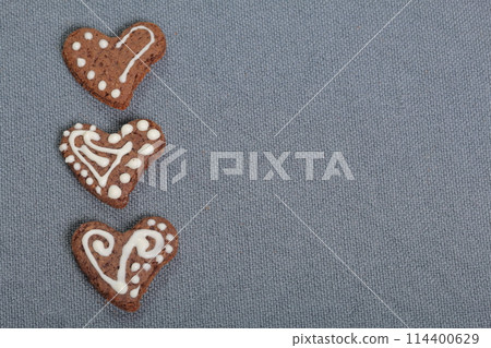 Gingerbread cookies decorated with a pattern of white glaze. On a background of gray fabric. 114400629