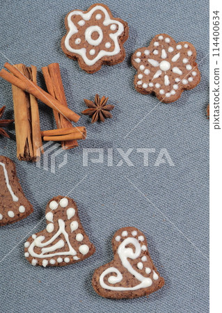 Gingerbread cookies decorated with a pattern of white glaze. On a background of gray fabric. Decorated with decorative elements of cinnamon sticks and anise stars. Gingerbread cookies decorated with a pattern of white glaze. On a background of gray fabric. Decorated with decorative elements of cinnamon sticks and anise stars. 114400634
