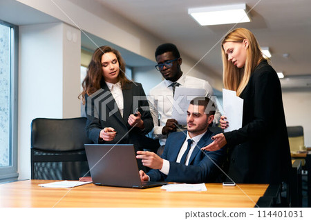 Multiethnic business team collaborates in office space, working on project with laptop. African and Caucasian men, women discuss strategies. Pro group engage in creative brainstorming. 114401031