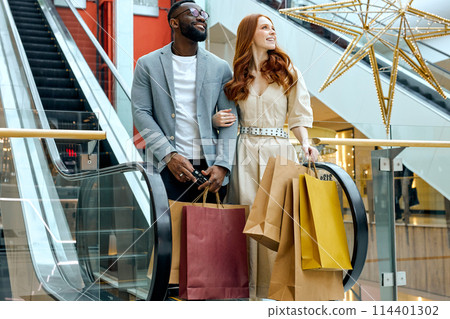 happy young man and woman looking up holding colourful bags 114401302