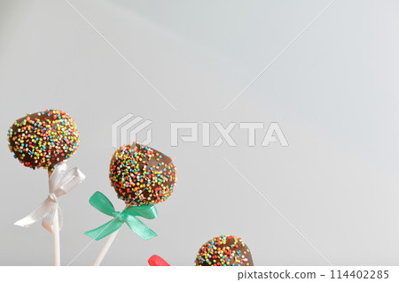 Cake Pops in chocolate with colored sprinkles. Decorated with a ribbon bow. On a white background. 114402285