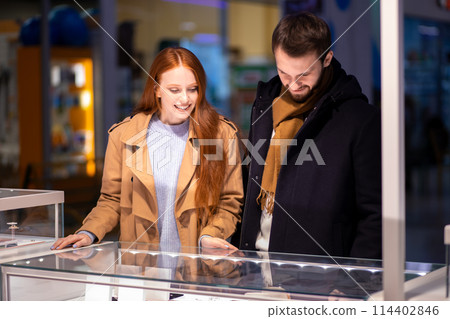 redhaired woman with male selects expensive jewelry at jeweler's shop redhaired woman with male selects expensive jewelry at jeweler's shop 114402846