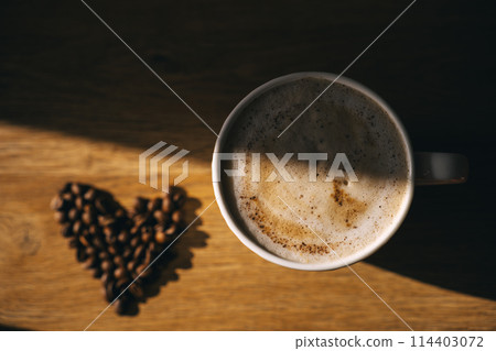 Cup of fresh cappuccino and coffee beans lying on the table in heart shape 114403072