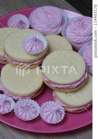 Cooked marshmallow sandwiches. They lie on plate. Next on the plate is a marshmallow of various sizes. 114403178